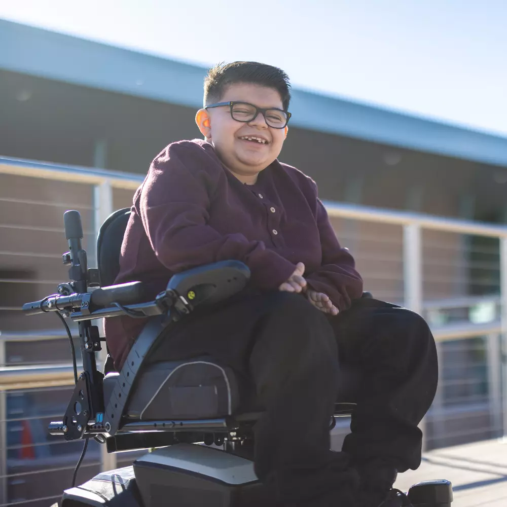 Smiling disabled boy in wheelchair with glasses