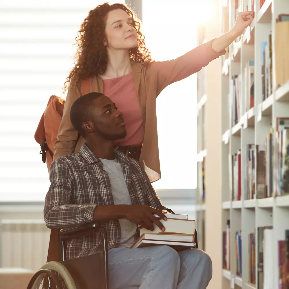 Disabled man in wheelchair with carer at library