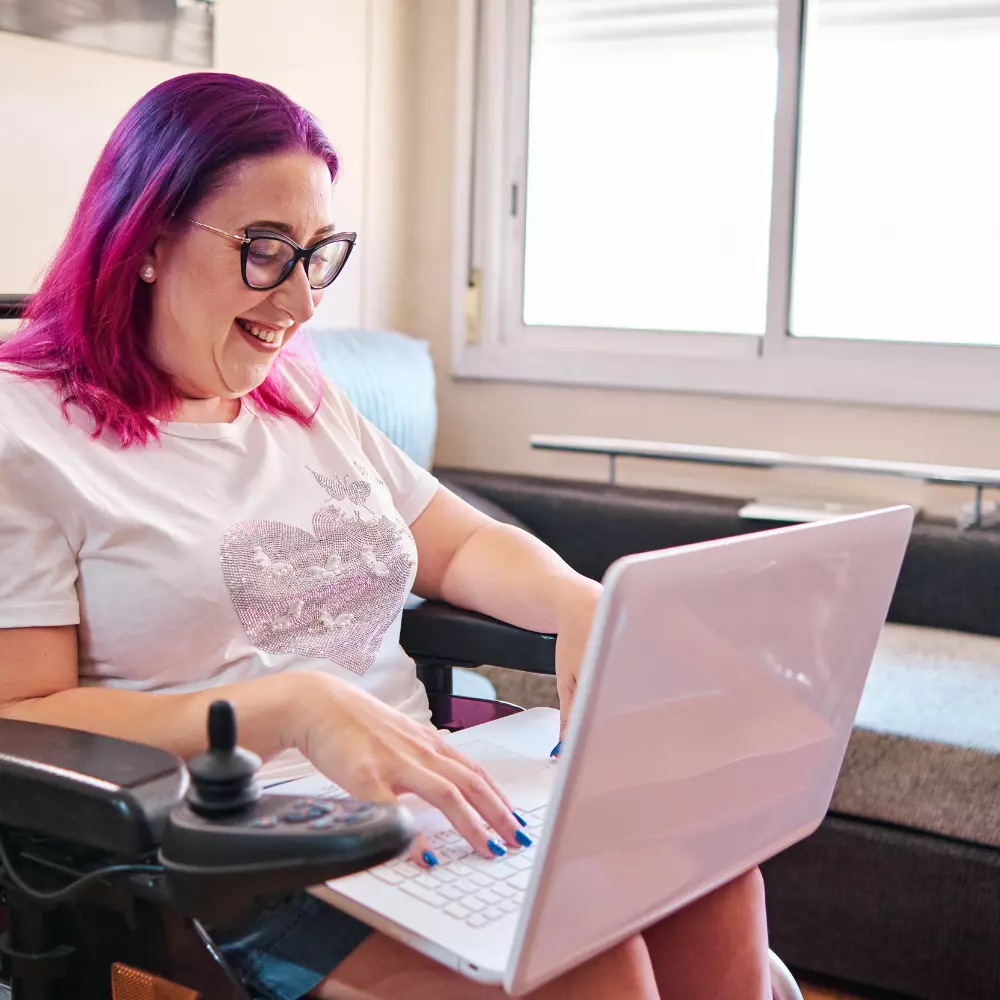 Woman in wheelchair smiling and working on laptop